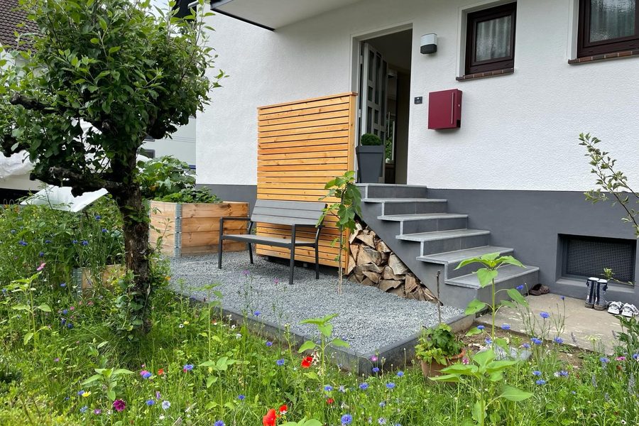 Sanierter Hauseingang mit neuer Treppe, Holz-Sichtschutz und Blumenwiese